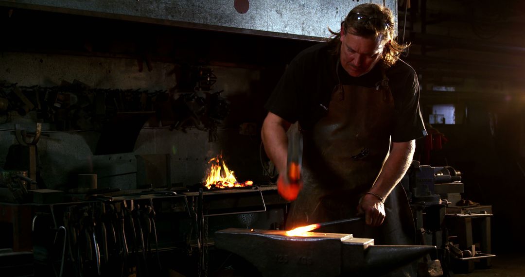 Blacksmith forging metal in dimly lit workshop - Free Images, Stock Photos and Pictures on Pikwizard.com