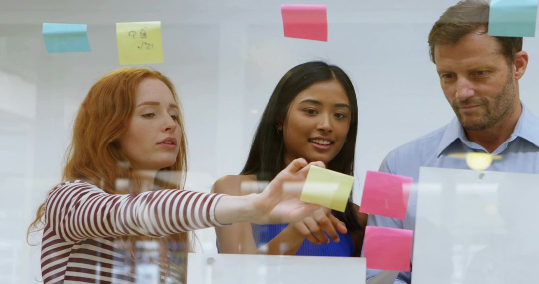 Collaborating at glass board placing sticky notes during team brainstorming session