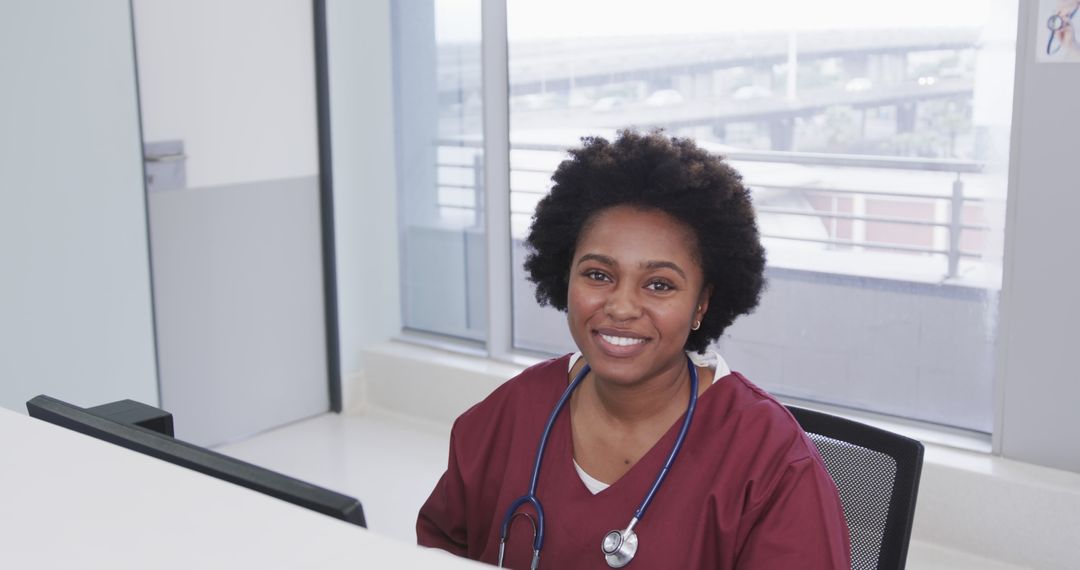 Smiling Nurse Wearing Scrubs and Stethoscope Sitting at Desk - Free Images, Stock Photos and Pictures on Pikwizard.com