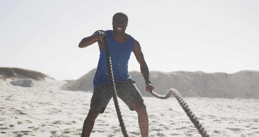 Smiling african american man exercising with battling ropes outdoors on beach - Free Images, Stock Photos and Pictures on Pikwizard.com