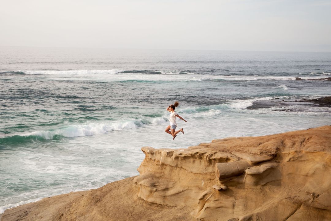 Woman Jumping on Sandy Cliffs by Oceanside - Free Images, Stock Photos and Pictures on Pikwizard.com