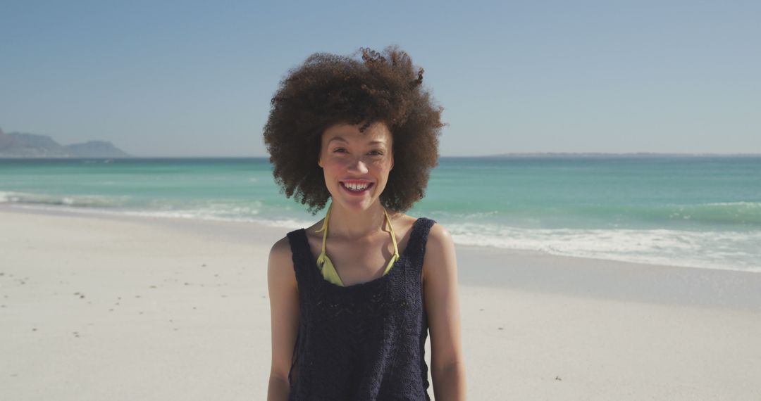 Portrait of laughing biracial woman with curly, brown hair, standing on beach - Free Images, Stock Photos and Pictures on Pikwizard.com
