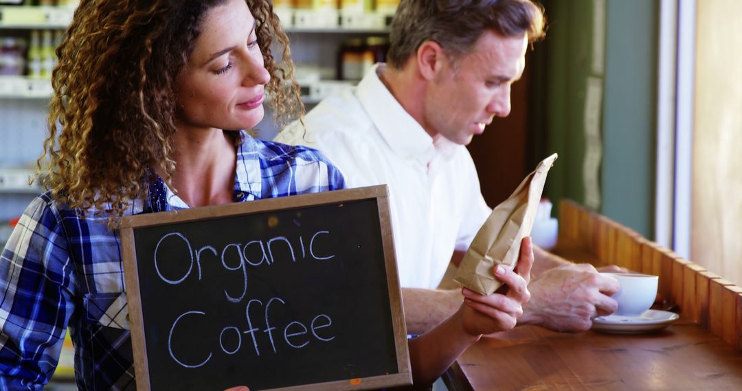 Female Barista Displaying Organic Coffee Sign in Cafe - Free Images, Stock Photos and Pictures on Pikwizard.com