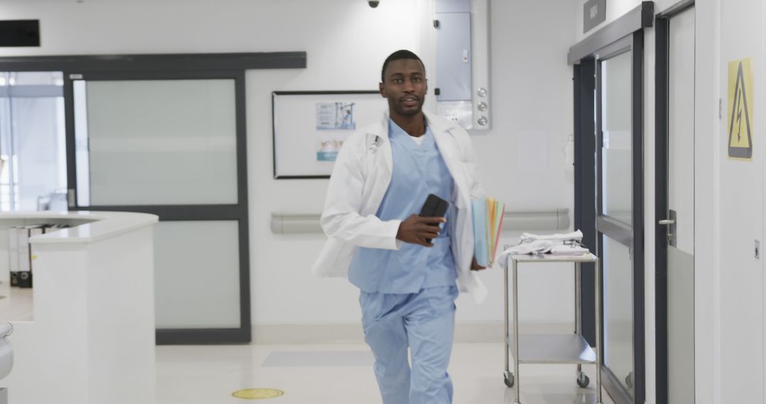 Confident Doctor Walking Quickly Through Hospital Corridor Holding Documents and Phone - Free Images, Stock Photos and Pictures on Pikwizard.com