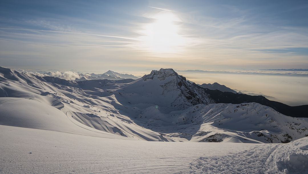 Sunlit jagged peak casting long shadows over alpine snowfield with tracks and contrail
