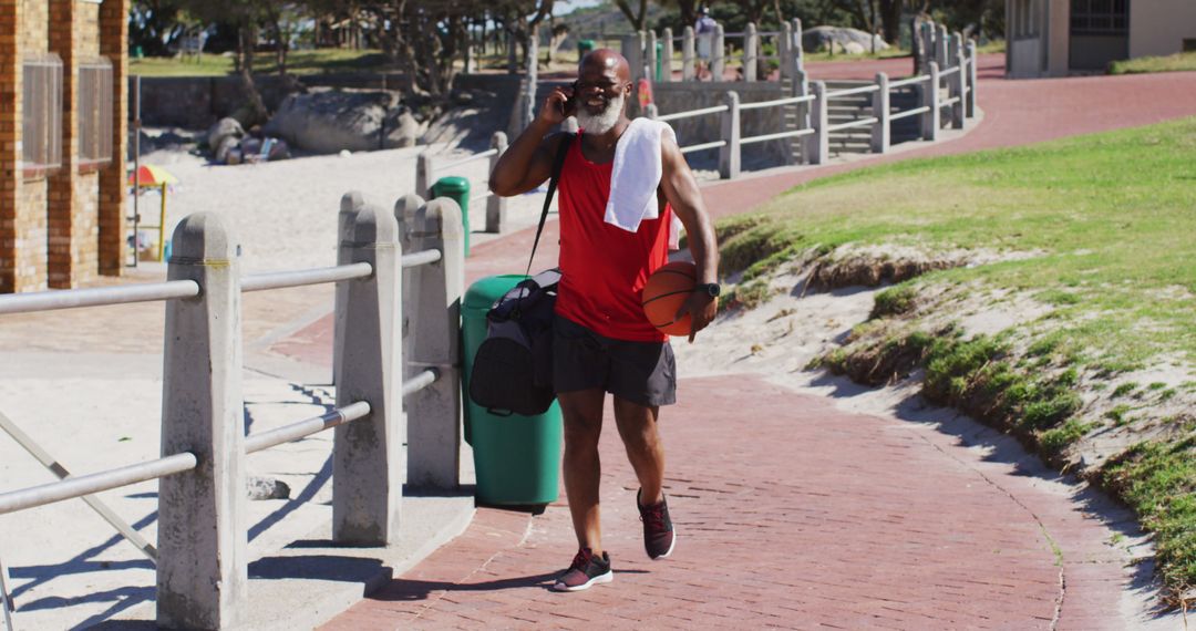 Senior Man Strolling by Beach with Basketball Talking on Phone