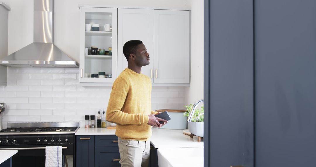 Man Looking Thoughtful in Modern Kitchen with Smartphone
