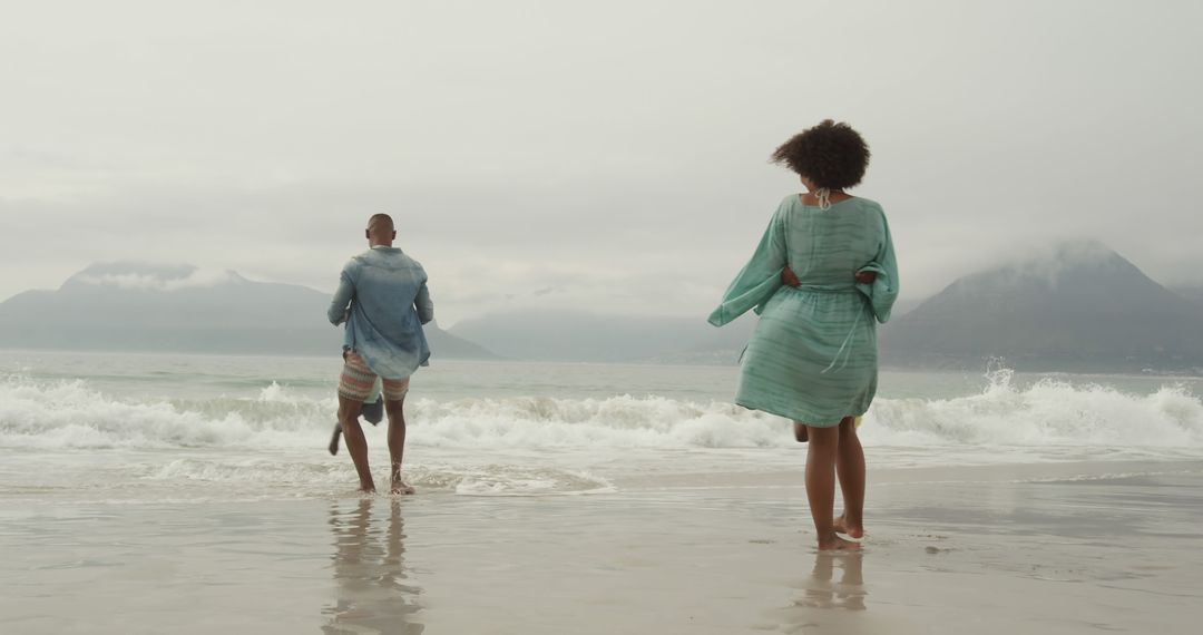 Couple Enjoying Walk on Beach with Mountain Background - Free Images, Stock Photos and Pictures on Pikwizard.com