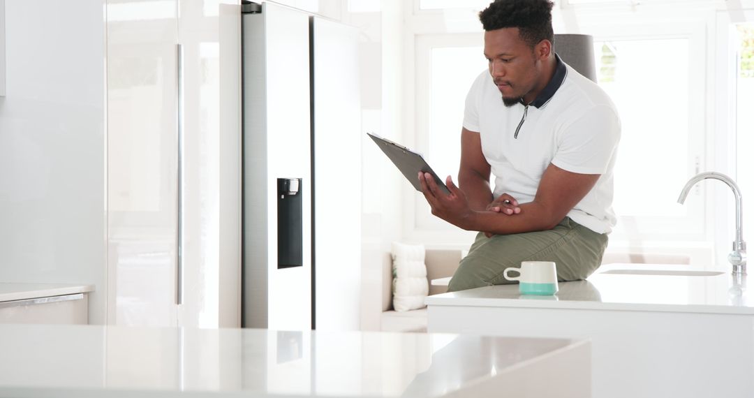 Man Writing on Clipboard in Modern Kitchen with Natural Light