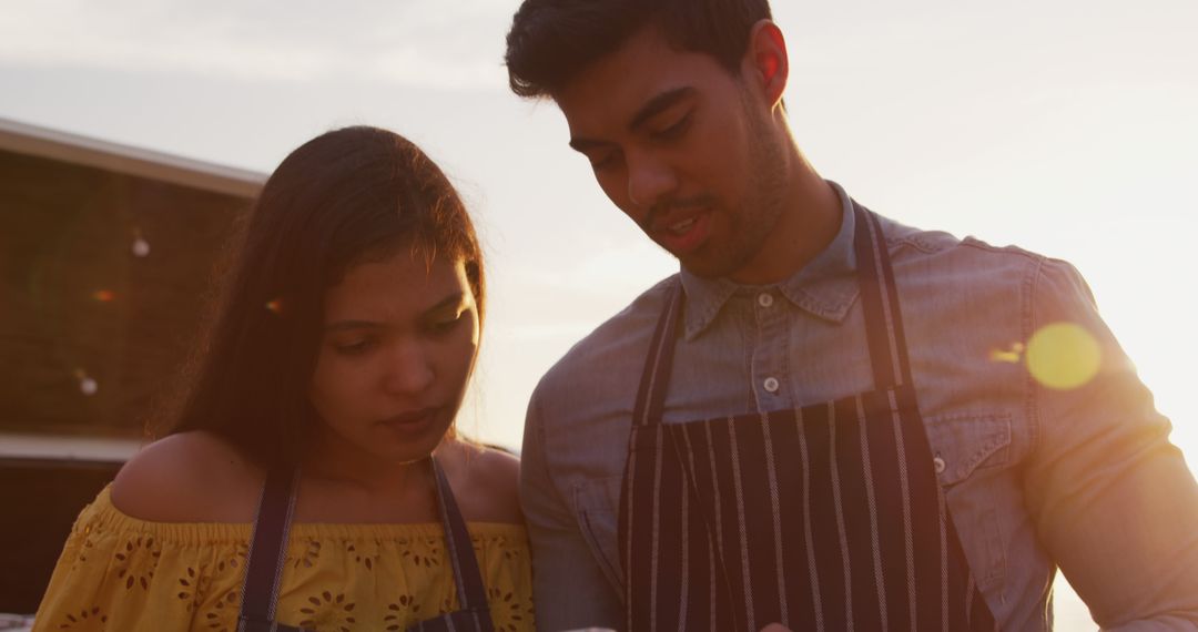 Diverse Couple in Aprons Cooking Outside at Sunset