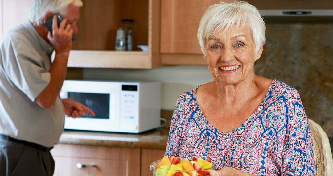 Elderly Woman Smiling while Holding Fruit Salad in Kitchen - Free Images, Stock Photos and Pictures on Pikwizard.com