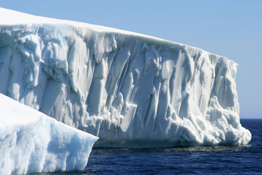 Massive Tabular Iceberg Towering Over Deep Blue Polar Ocean With Sheer Ice Cliff