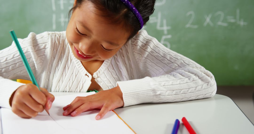 Asian girl enjoying drawing in classroom with green chalkboard background - Free Images, Stock Photos and Pictures on Pikwizard.com