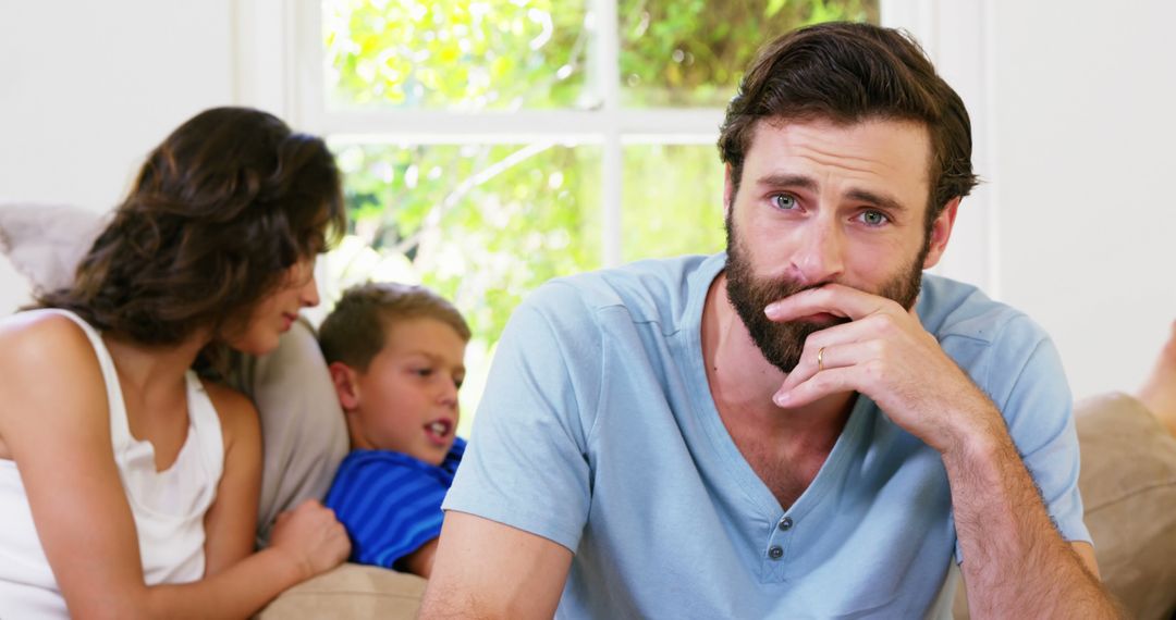 Stressed Man Sitting on Couch with Family in Background - Free Images, Stock Photos and Pictures on Pikwizard.com