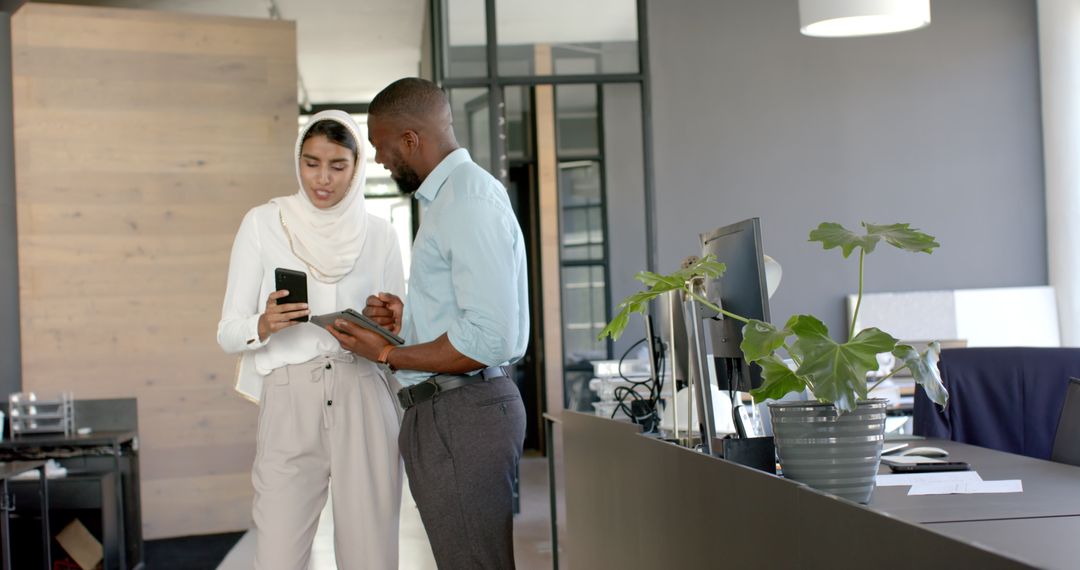 Professional Colleagues Discussing Work on Digital Devices in Modern Office