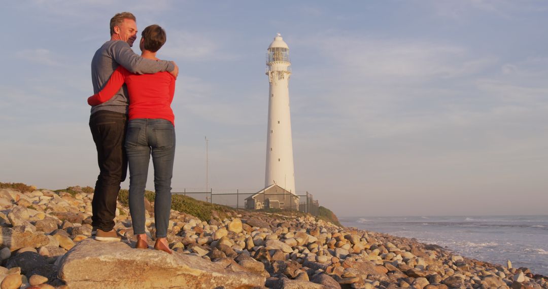 Couple Embracing by Ocean Side Lighthouse During Sunset - Free Images, Stock Photos and Pictures on Pikwizard.com