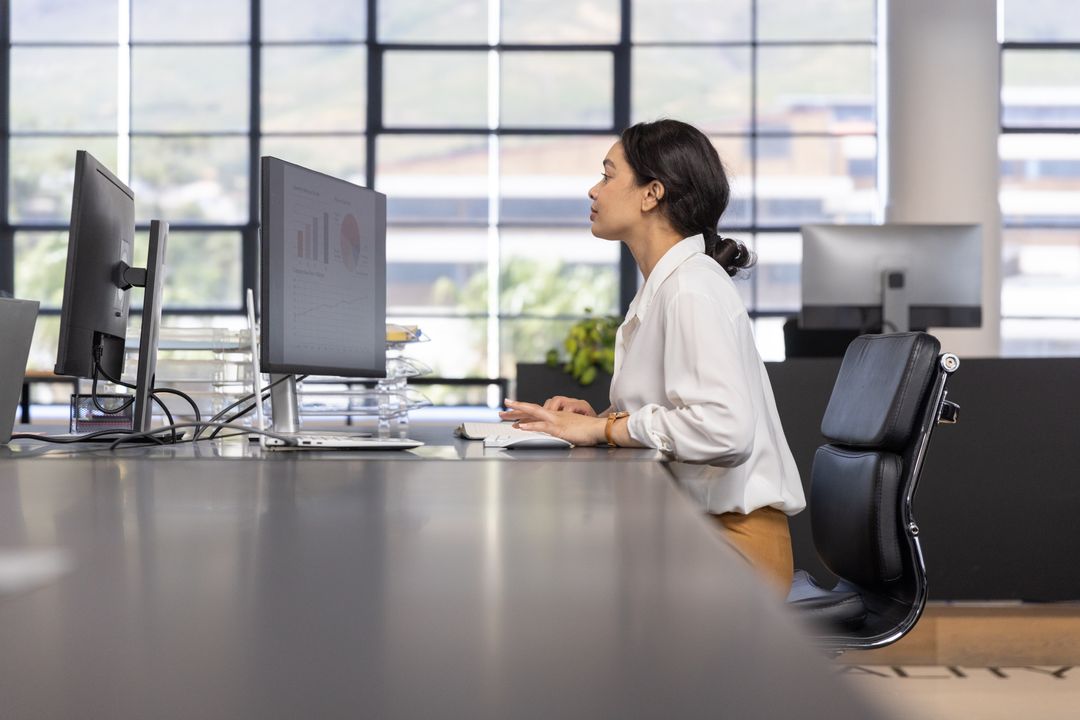 Professional Woman Analyzing Data on Multiple Screens in Office