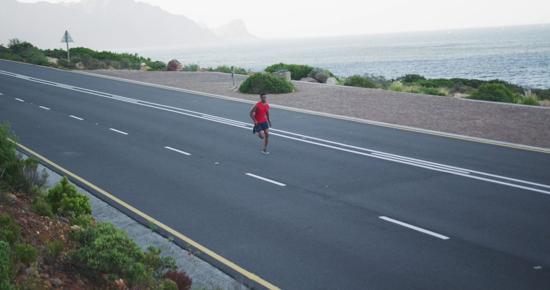 African american man exercising outdoors running on a coastal road - Free Images, Stock Photos and Pictures on Pikwizard.com