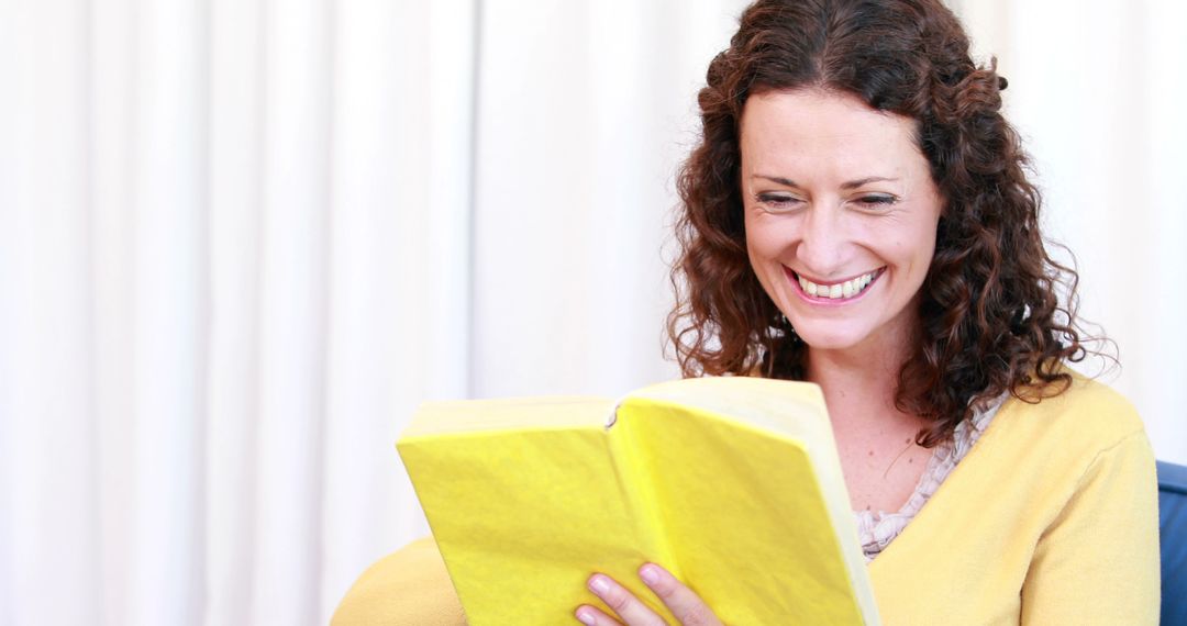 Smiling Woman Reading Yellow Book Relaxing on Chair Indoors - Free Images, Stock Photos and Pictures on Pikwizard.com