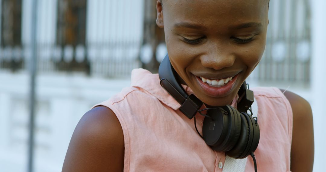 Young woman smiling with headphones around neck outdoors - Free Images, Stock Photos and Pictures on Pikwizard.com