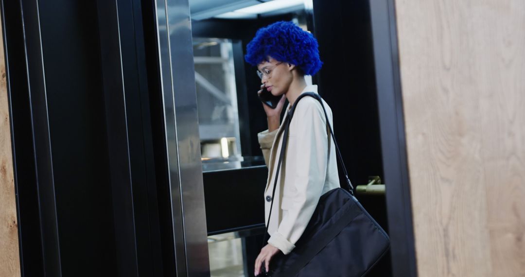Biracial casual businesswoman with blue afro talking on smartphone in office elevator - Free Images, Stock Photos and Pictures on Pikwizard.com