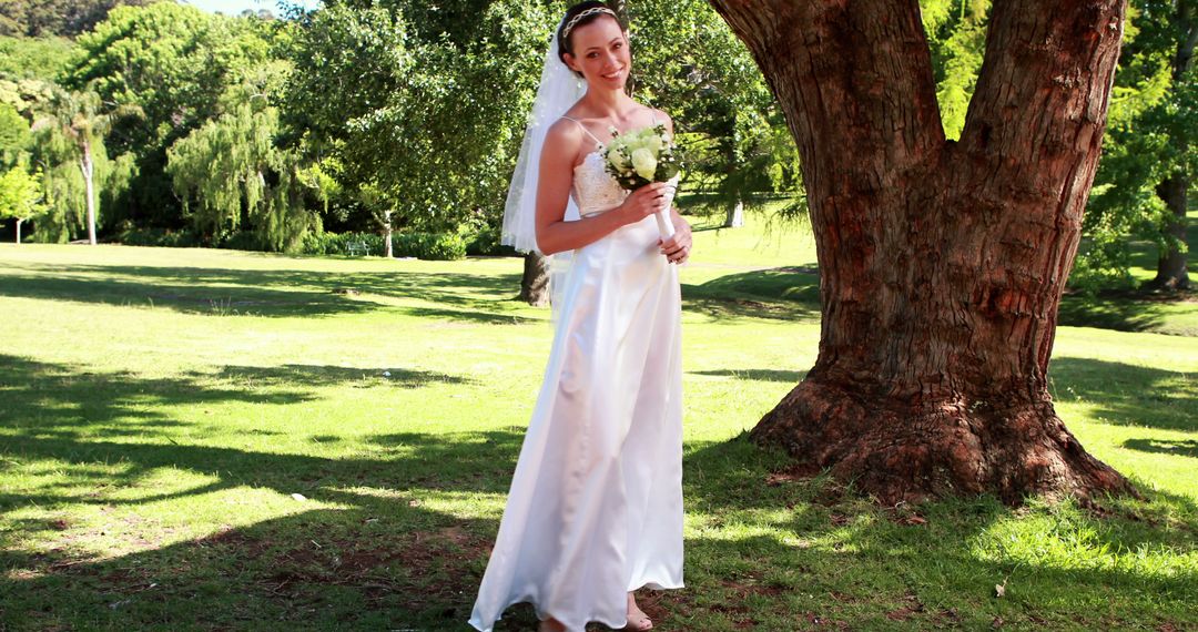 Smiling Bride Holding Bouquet in Outdoor Park Under Tree - Free Images, Stock Photos and Pictures on Pikwizard.com