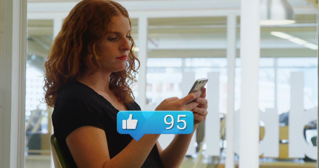 Redhead woman tapping smartphone in modern office with social media like notification