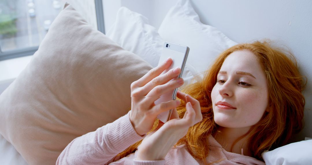 Relaxed Redheaded Woman Using Smartphone on Bed - Free Images, Stock Photos and Pictures on Pikwizard.com