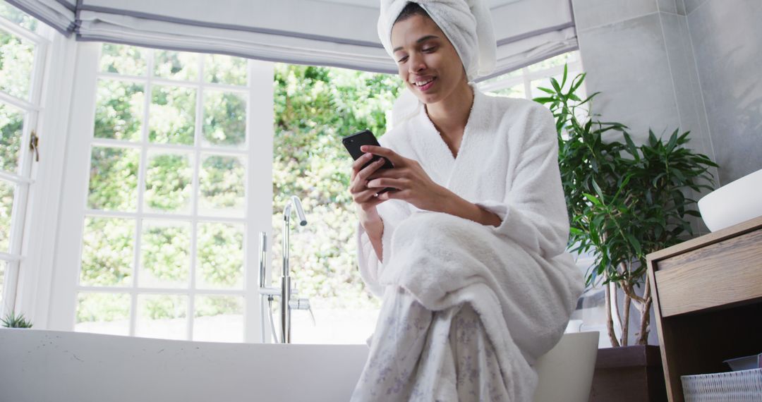 Relaxed Young Woman In Bathrobe Using Smartphone While Sitting On Bathtub Edge - Free Images, Stock Photos and Pictures on Pikwizard.com