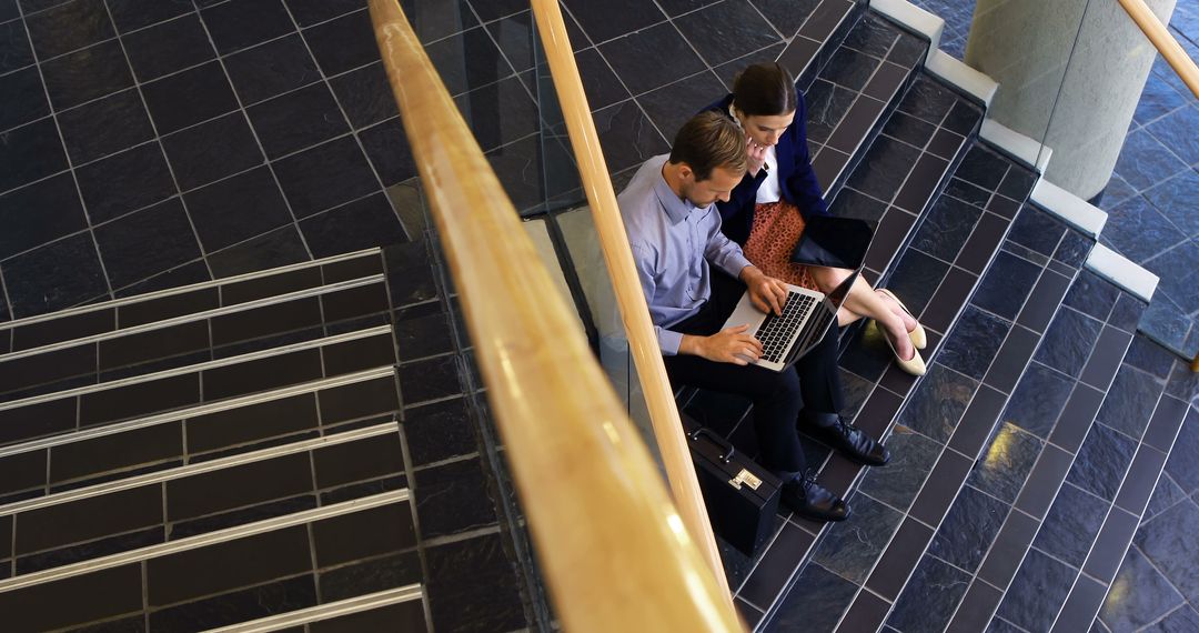 Young Professionals Collaborating on Laptop in Office Stairwell