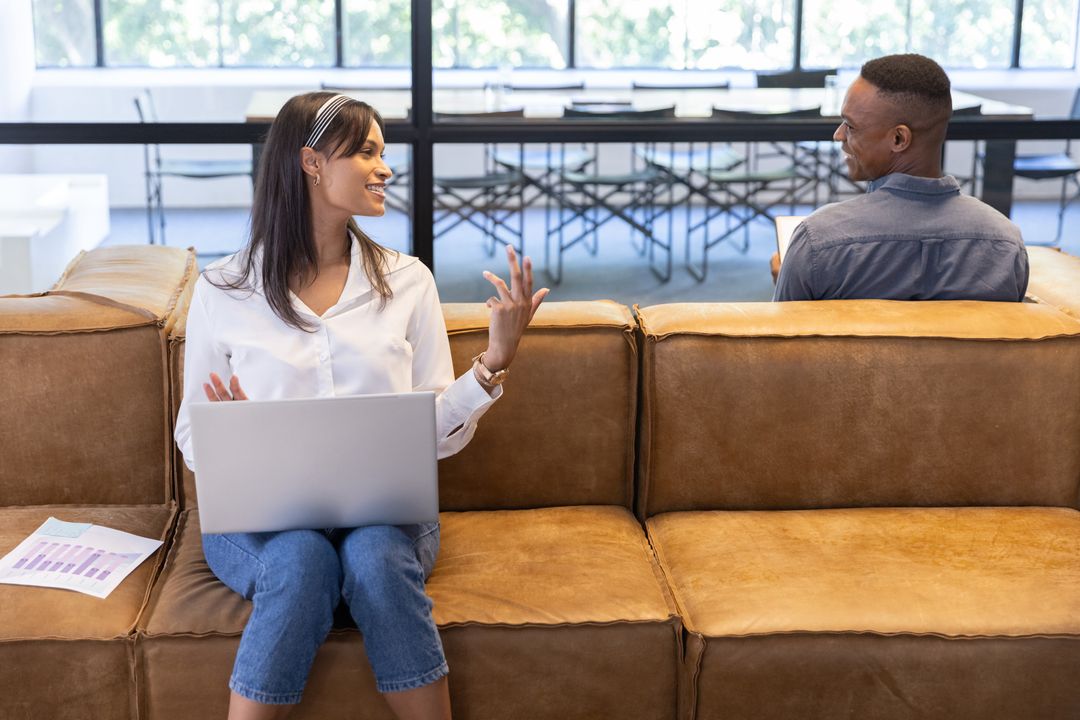 Diverse coworkers collaborating on laptop in modern office lounge for relaxed teamwork