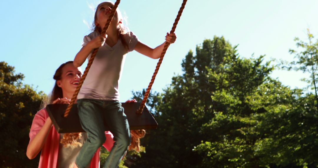 Little girl being pushed on a swing by her mother in the park on a sunny day - Free Images, Stock Photos and Pictures on Pikwizard.com