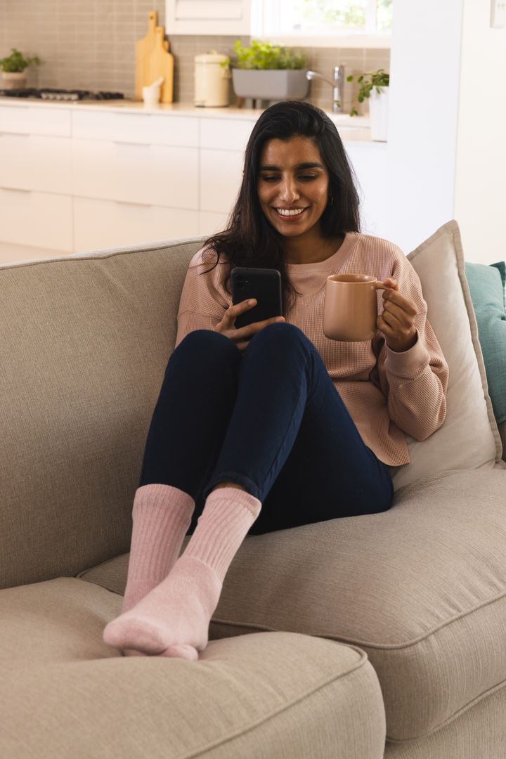 Relaxed Woman Sitting on Sofa with Smartphone and Coffee Mug