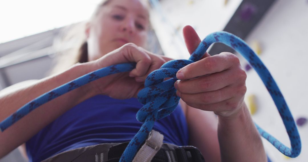 Low angle view of caucasian woman knotting rope in a harness belt at indoor climbing wall - Free Images, Stock Photos and Pictures on Pikwizard.com