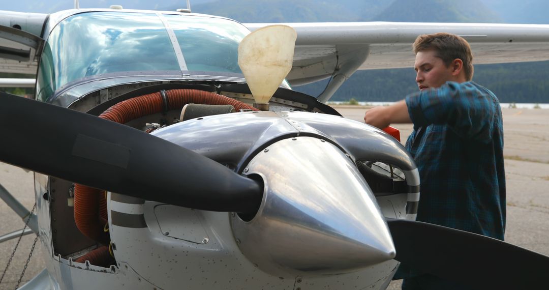 Young Man Inspecting Small Aircraft Engine on Runway