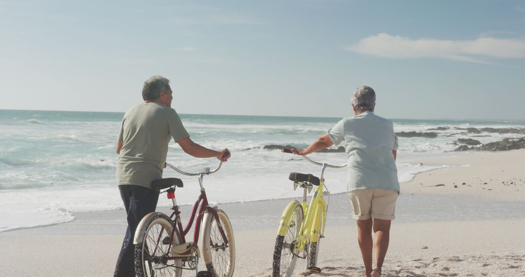 Senior Couple Walking with Bicycles on Beach Near Ocean