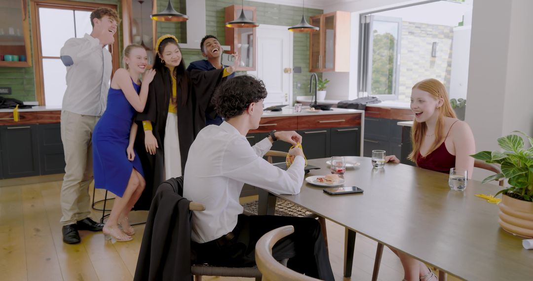Diverse graduates celebrating in modern open-plan kitchen posing for selfie and laughing
