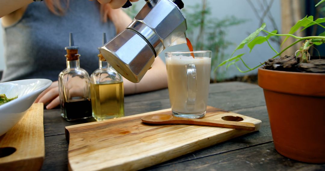 Person Pouring Fresh Coffee into a Mug on Wooden Board with Potted Plant in Background - Free Images, Stock Photos and Pictures on Pikwizard.com