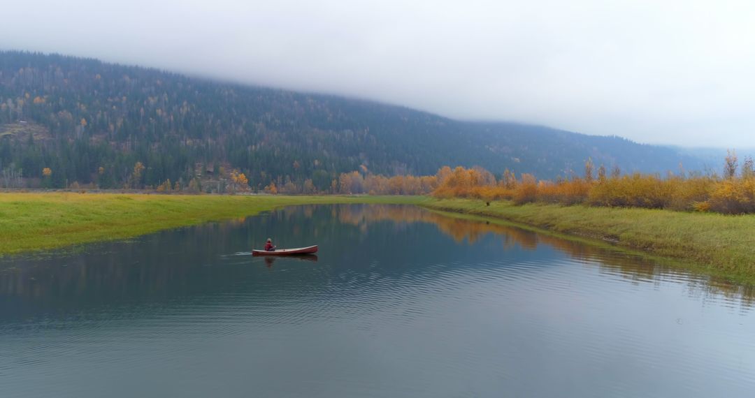Man Kayaking on Calm Autumn River with Misty Mountains