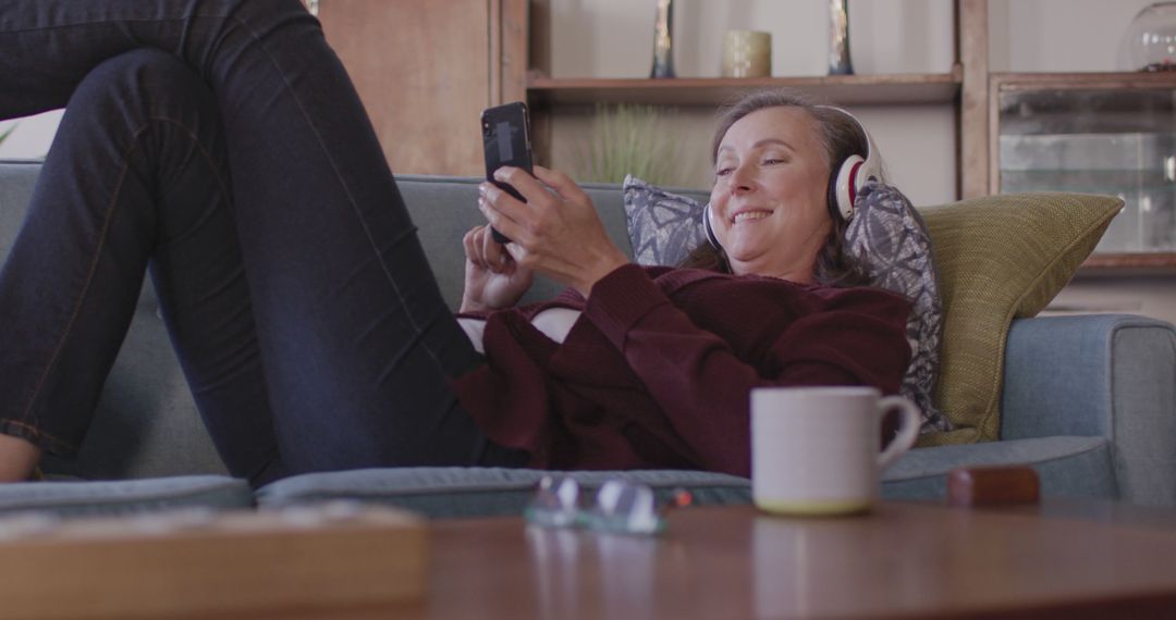 Woman Relaxing on Couch Wearing Headphones Using Smartphone - Free Images, Stock Photos and Pictures on Pikwizard.com