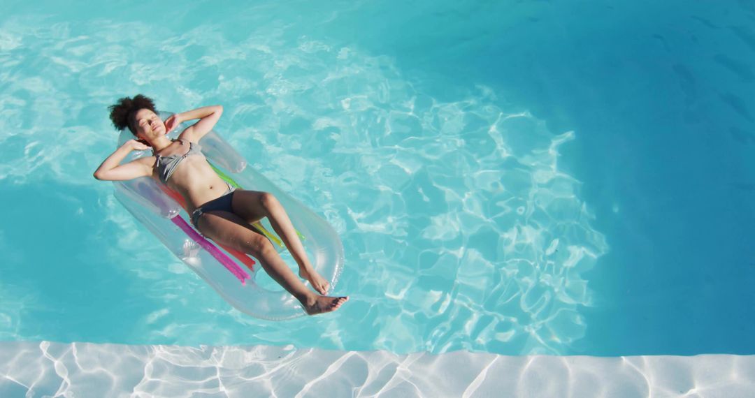 Young woman floating on inflatable lounger in turquoise pool relaxing summer lifestyle
