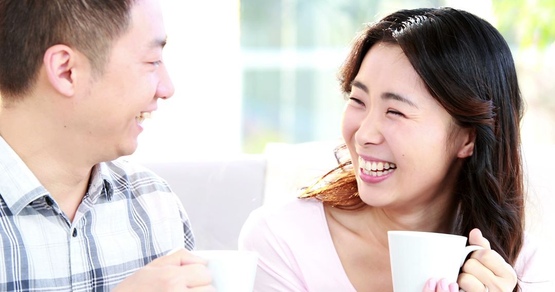 An Asian man and woman share a joyful moment over coffee, with copy space - Free Images, Stock Photos and Pictures on Pikwizard.com
