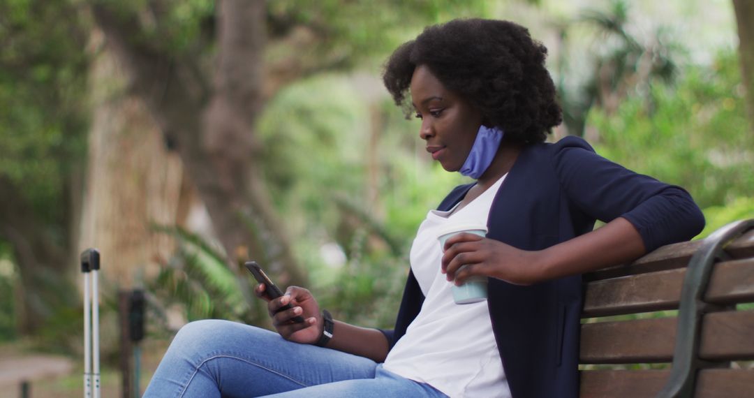 African American Woman Relaxing on Park Bench Holding Coffee Using Smartphone - Free Images, Stock Photos and Pictures on Pikwizard.com