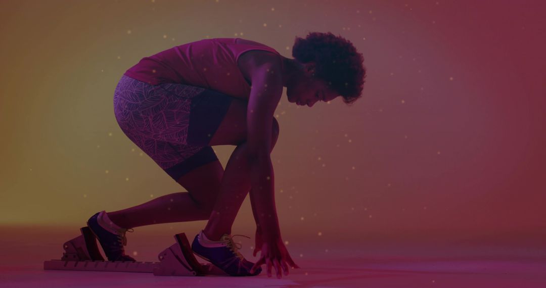 Sprinter crouching on starting block powering forward with track spikes and athletic wear