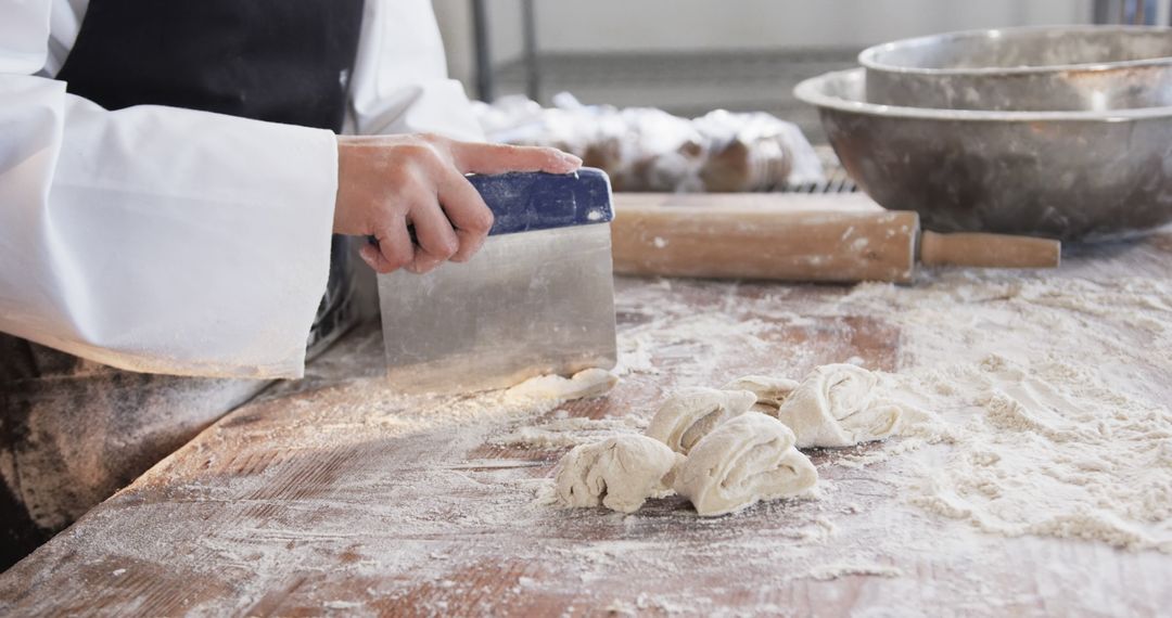 Baker slicing dough on floured wooden table in bakery - Free Images, Stock Photos and Pictures on Pikwizard.com