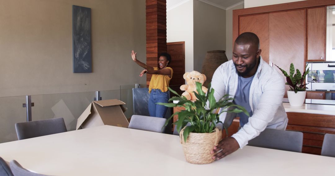 African American couple unpacking and placing woven planter with teddy on dining table during move