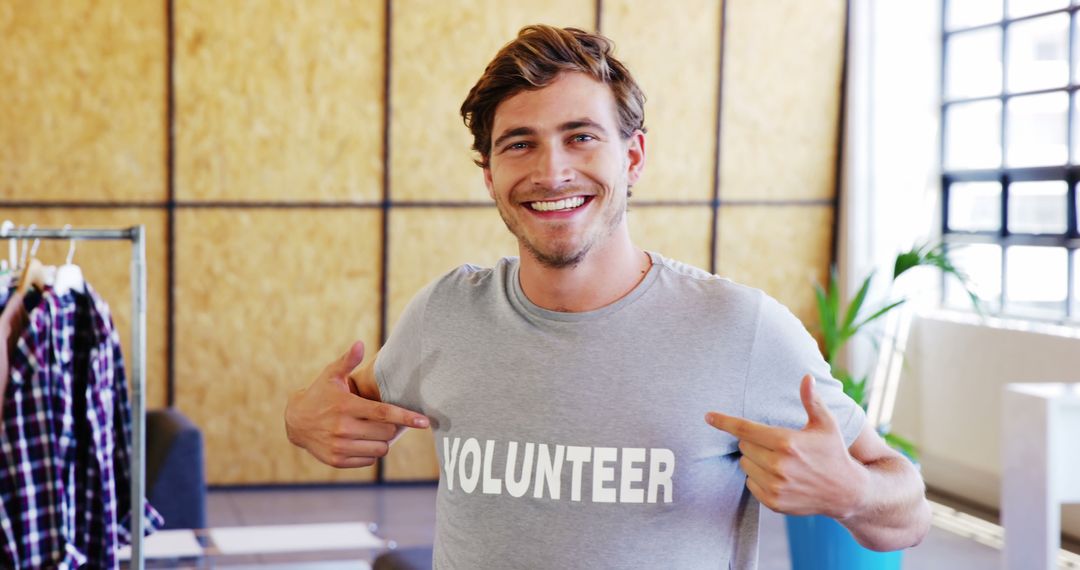 Smiling Male Volunteer Proudly Pointing at Shirt in Modern Office - Free Images, Stock Photos and Pictures on Pikwizard.com