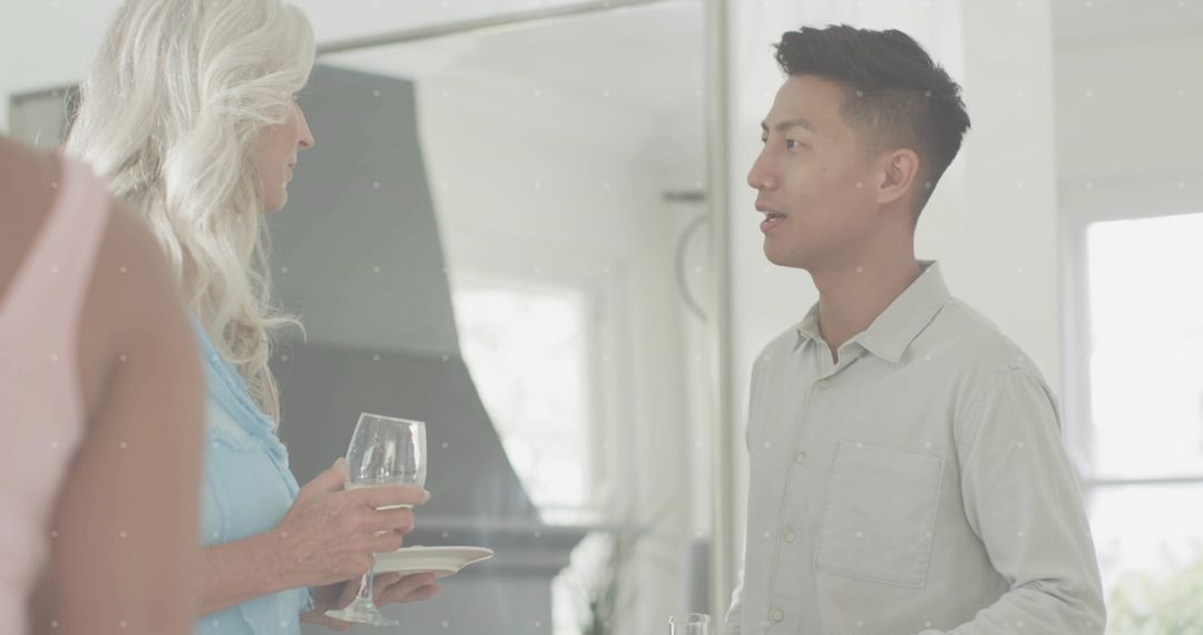 Asian man conversing with guest in modern kitchen during casual home entertaining with wine glass