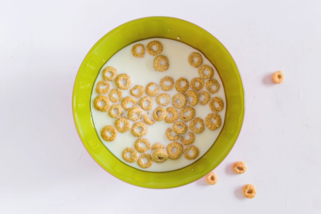 Top-down view of cereal rings floating in milk in green bowl on clean white background
