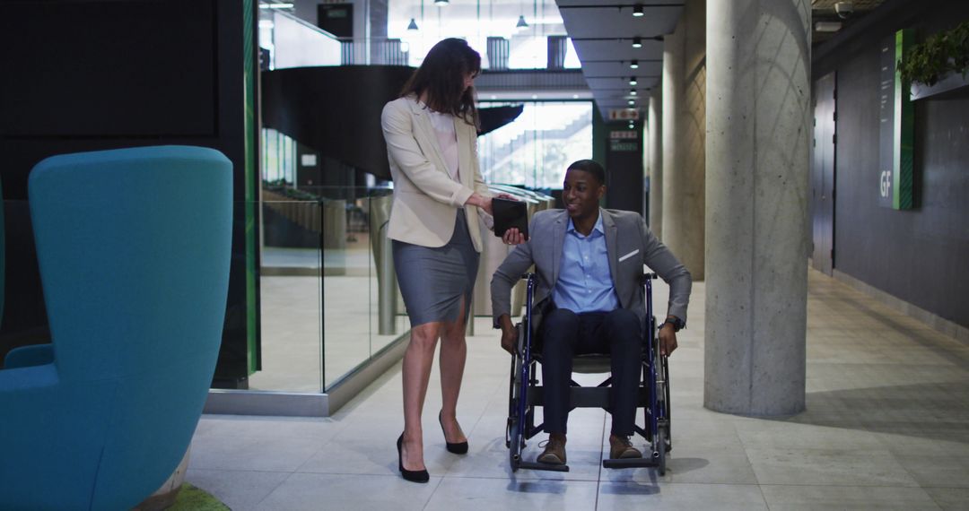 Business Professional Helping Colleague in a Wheelchair in Modern Office - Free Images, Stock Photos and Pictures on Pikwizard.com